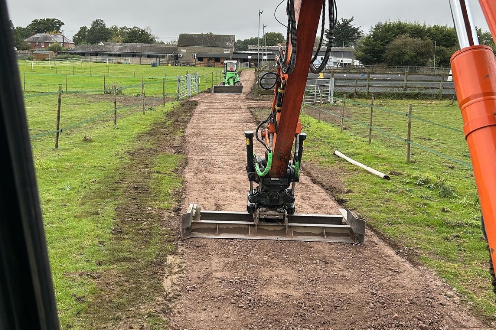 Excavator with a grading beam forming a new stone access track between paddocks at a Surrey farm