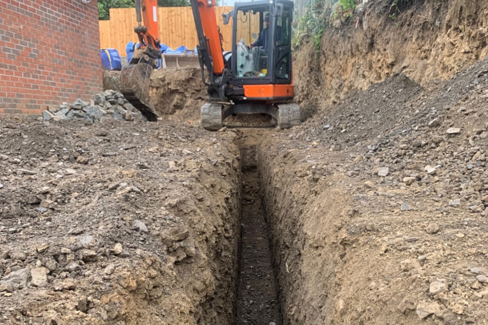 Groundworks contractor excavating a foundation trench on a site near Epsom