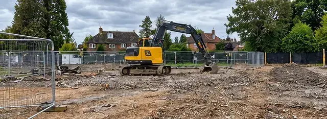 Excavator on a cleared development site behind temporary fencing