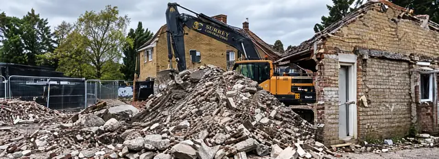 Surrey Contracting excavator demolishing a brick building, with rubble in the foreground