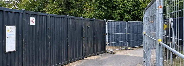 Black site hoarding with signage and temporary mesh fencing at a site entrance