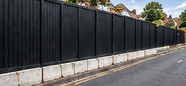 Black hoarding mounted on concrete blocks beside a road